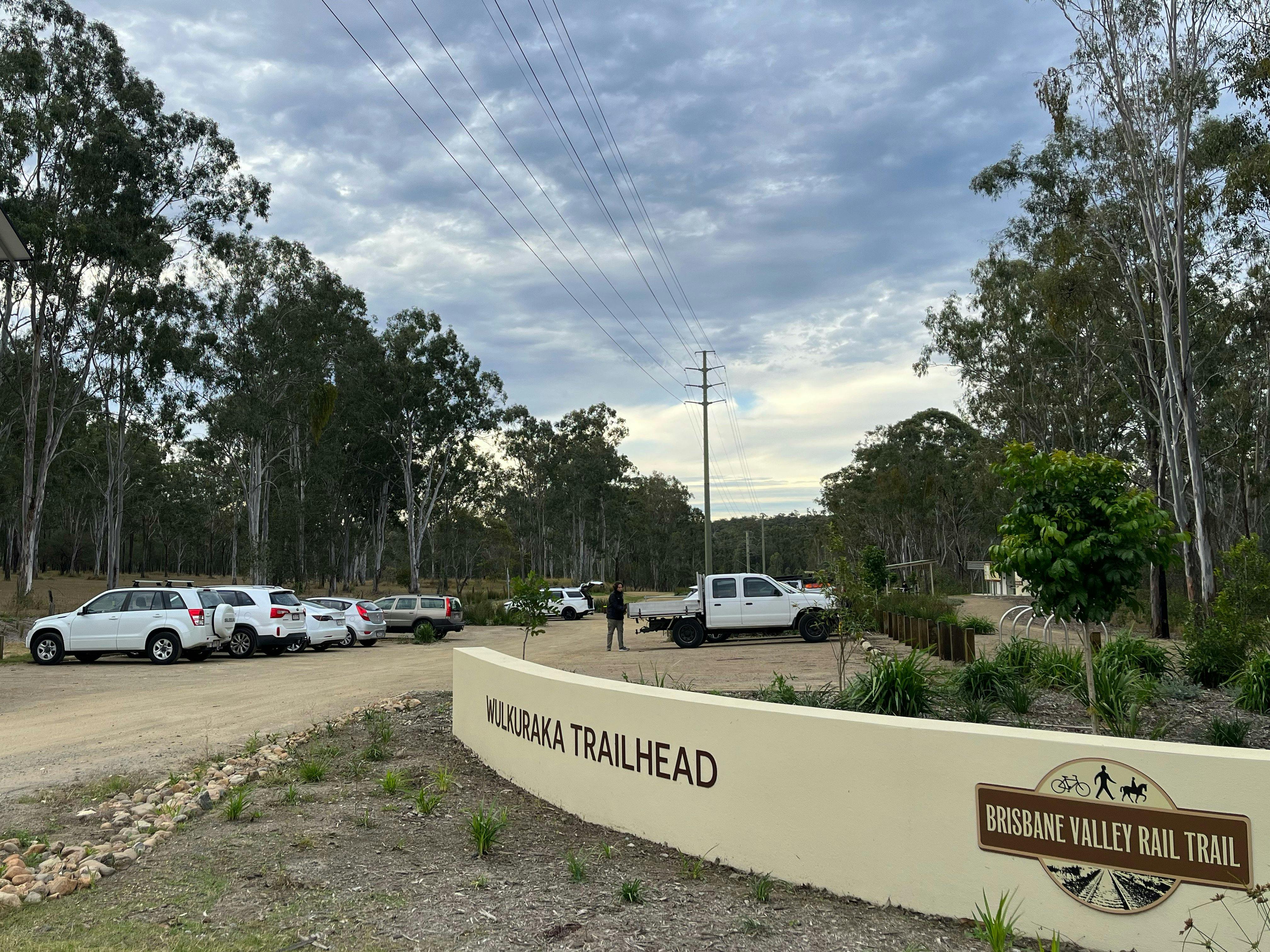 a  wall with the words Wulkuraka Trailhead & the BVRT logo, cars are parked in the background