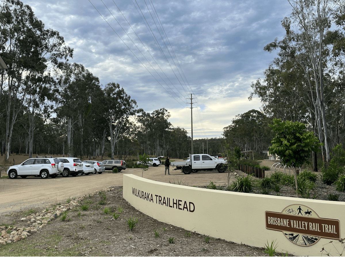 a  wall with the words Wulkuraka Trailhead & the BVRT logo, cars are parked in the background