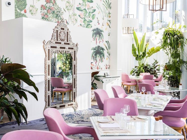 Image of pink chairs around tables that are set for dinner, a large mirror in the background