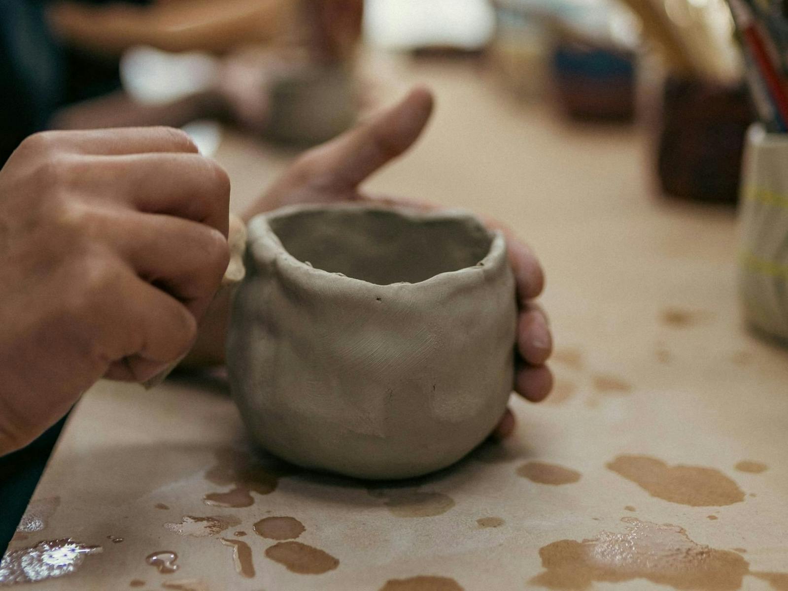 A hand sculpting a ceramic mug