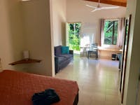 Motel style room showing edge of queen bed, sofa, tiled floor and green rainforest out back door