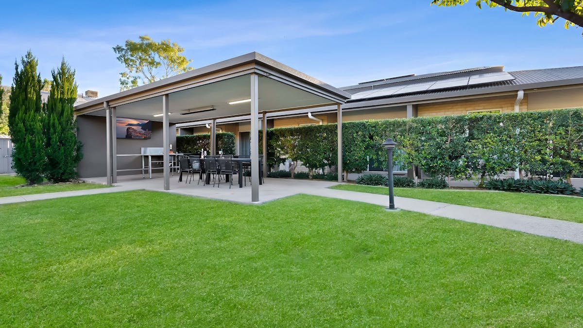 The Emerald Inn BBQ area with a flat screen TV, BBQ facilities, dining table and lawn area.