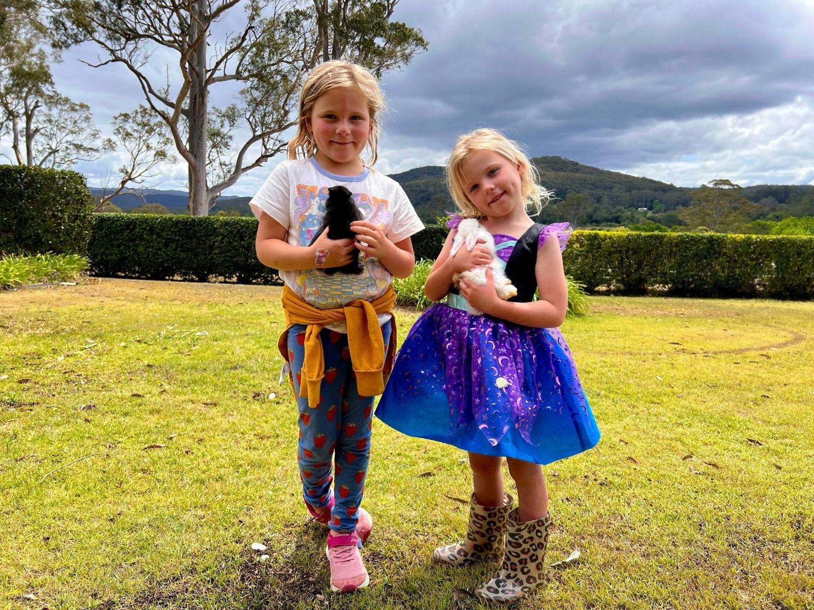Two young girls smiling and gently holding fluffy bunnies on the farm tour
