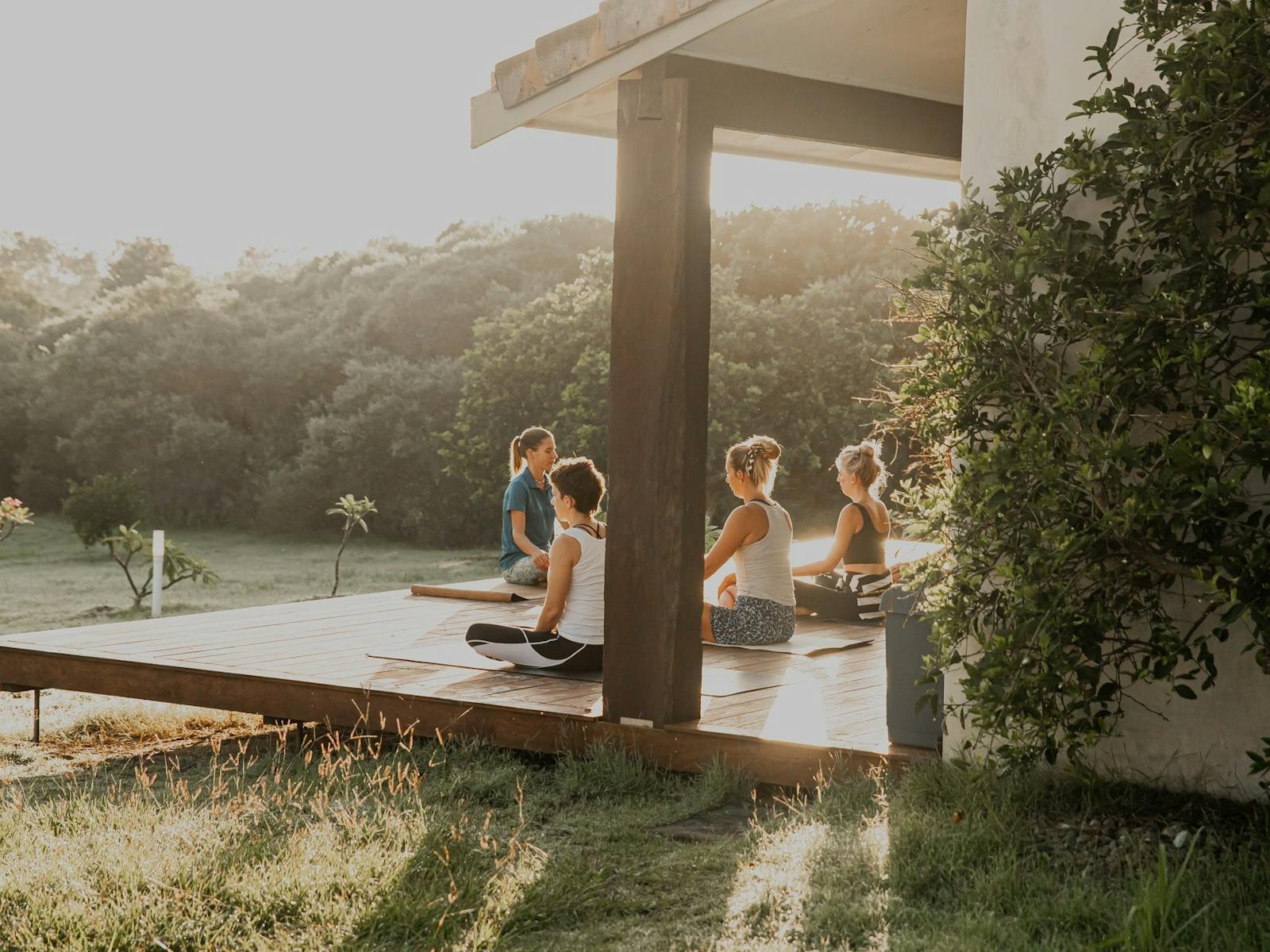 four women doing yoga on a timber platform overlooking a field