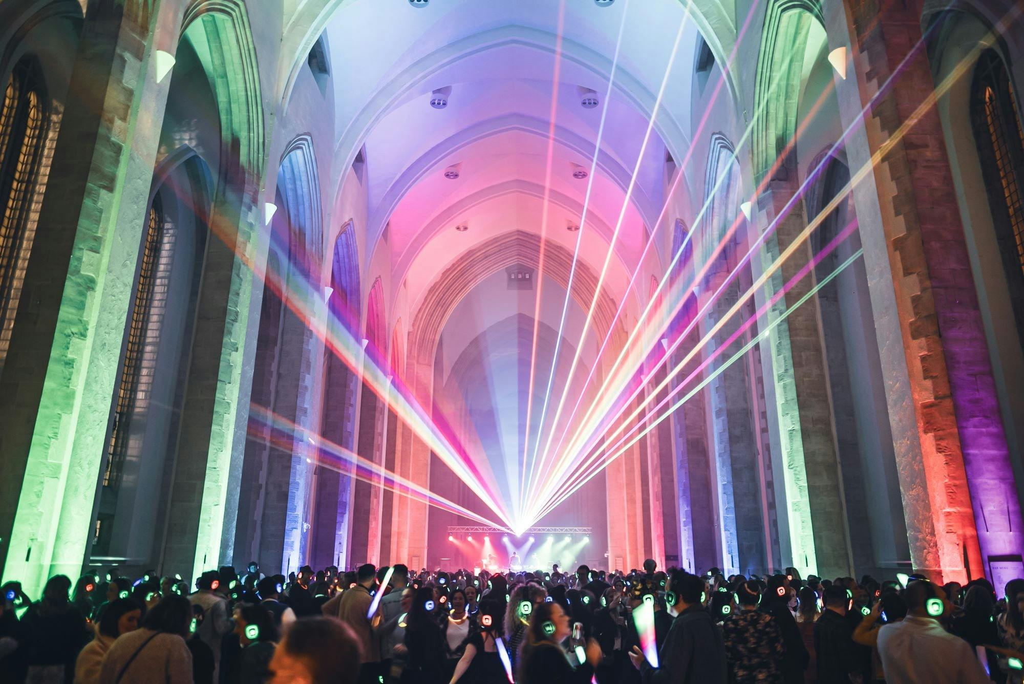 Crowd dancing to a silent disco in a hall with light show displayed above them