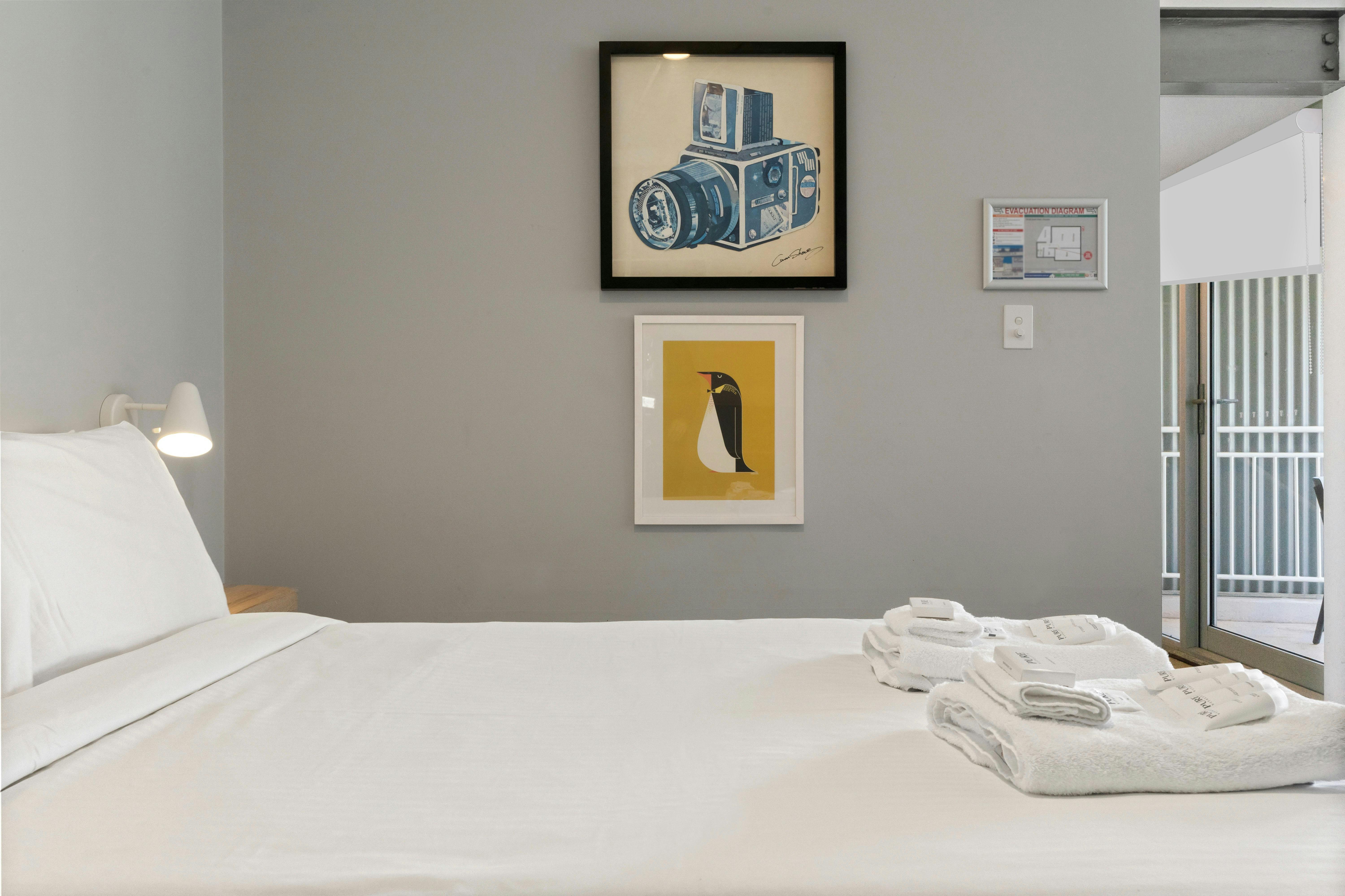 액자에 넣은 예술 작품과 흰색 리넨으로 꾸며진 아늑한 침실. 발코니에서 자연광이 들어옵니다.