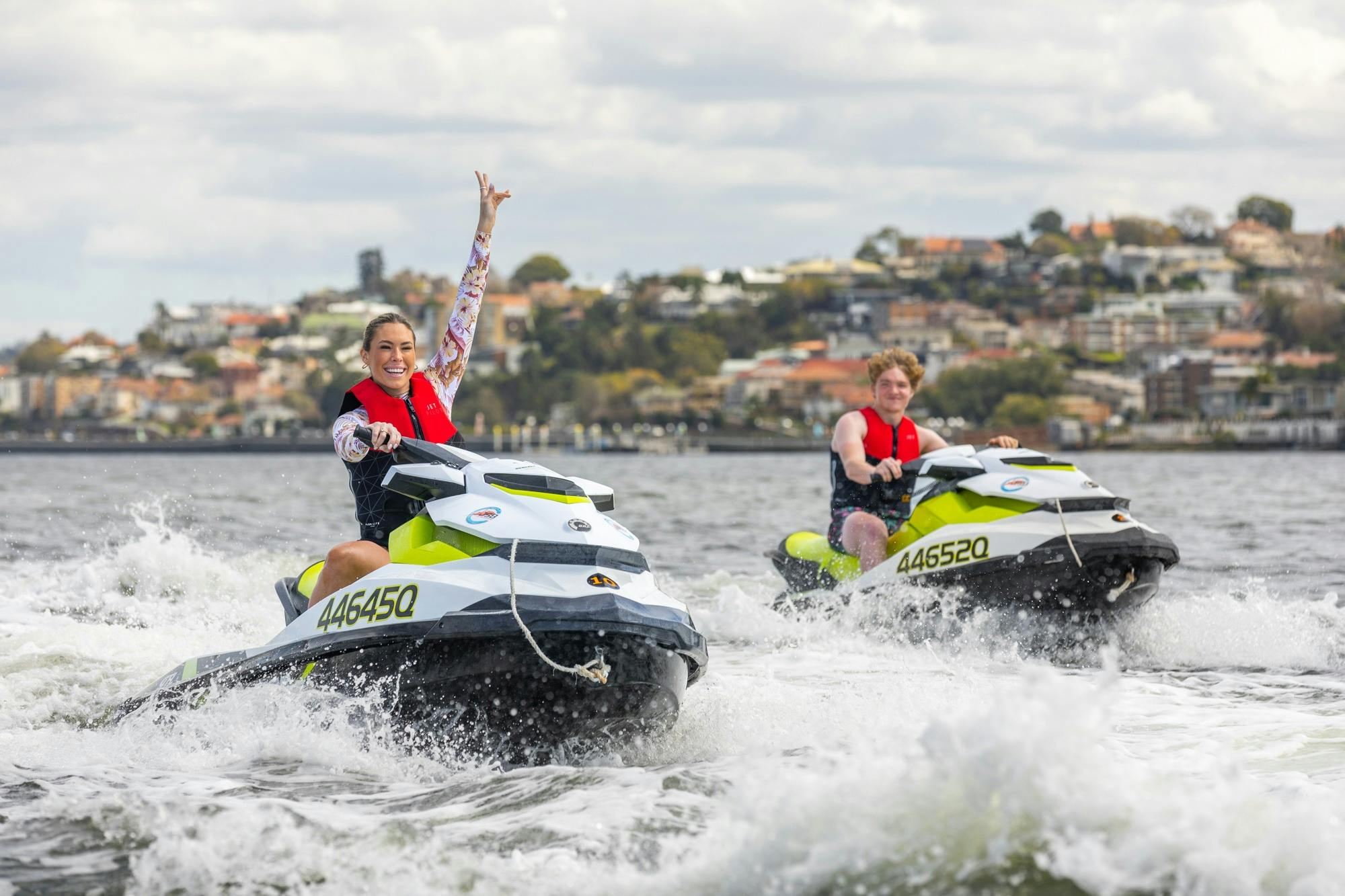 A couple cruising through the Brisbane River with arms in the air looking excited.