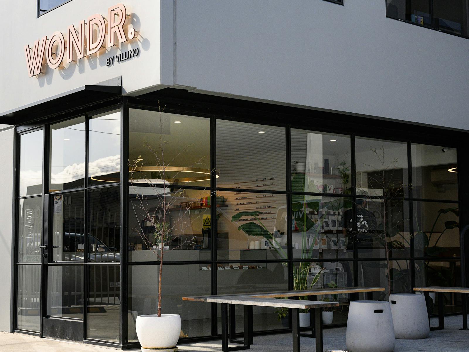 Outdoor seating at a modern cafe featuring floor to ceiling windows creating a sleek entrance.