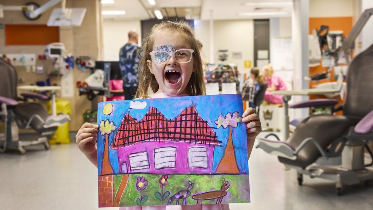 A child in hospital holding a drawing of a house