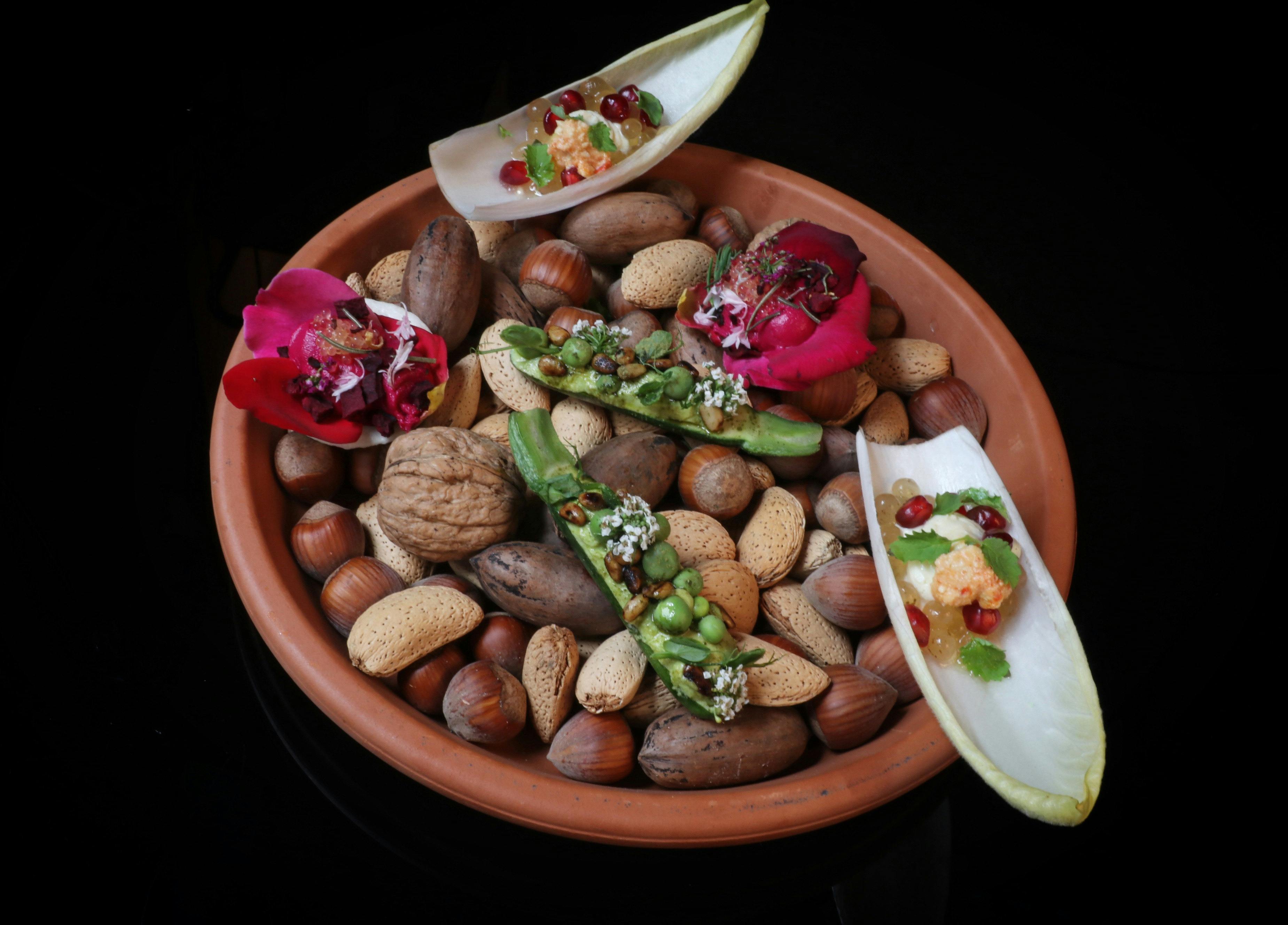 A terracotta dish filled with assorted nuts and topped with colourful bite-sized degustation dishes