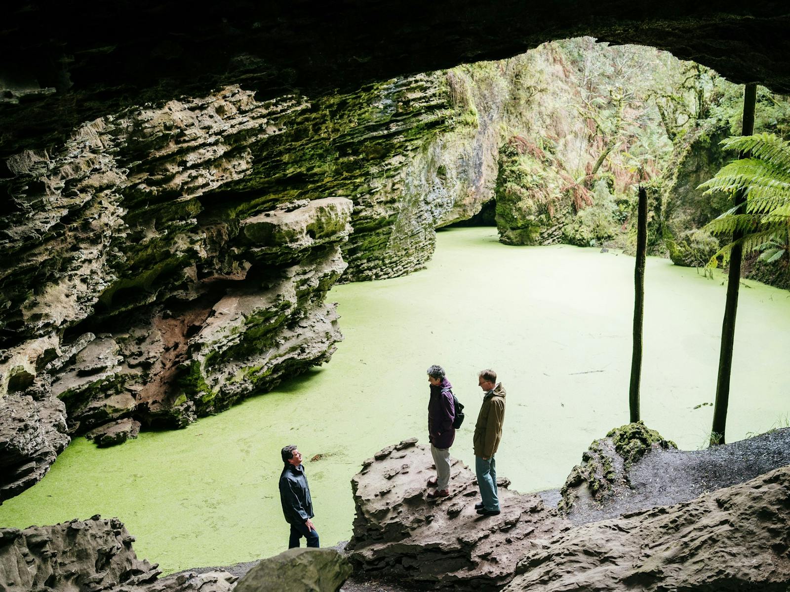 Couple at Trowutta Arch with tour guide. Algae swirling on surface of the water amidst rocks