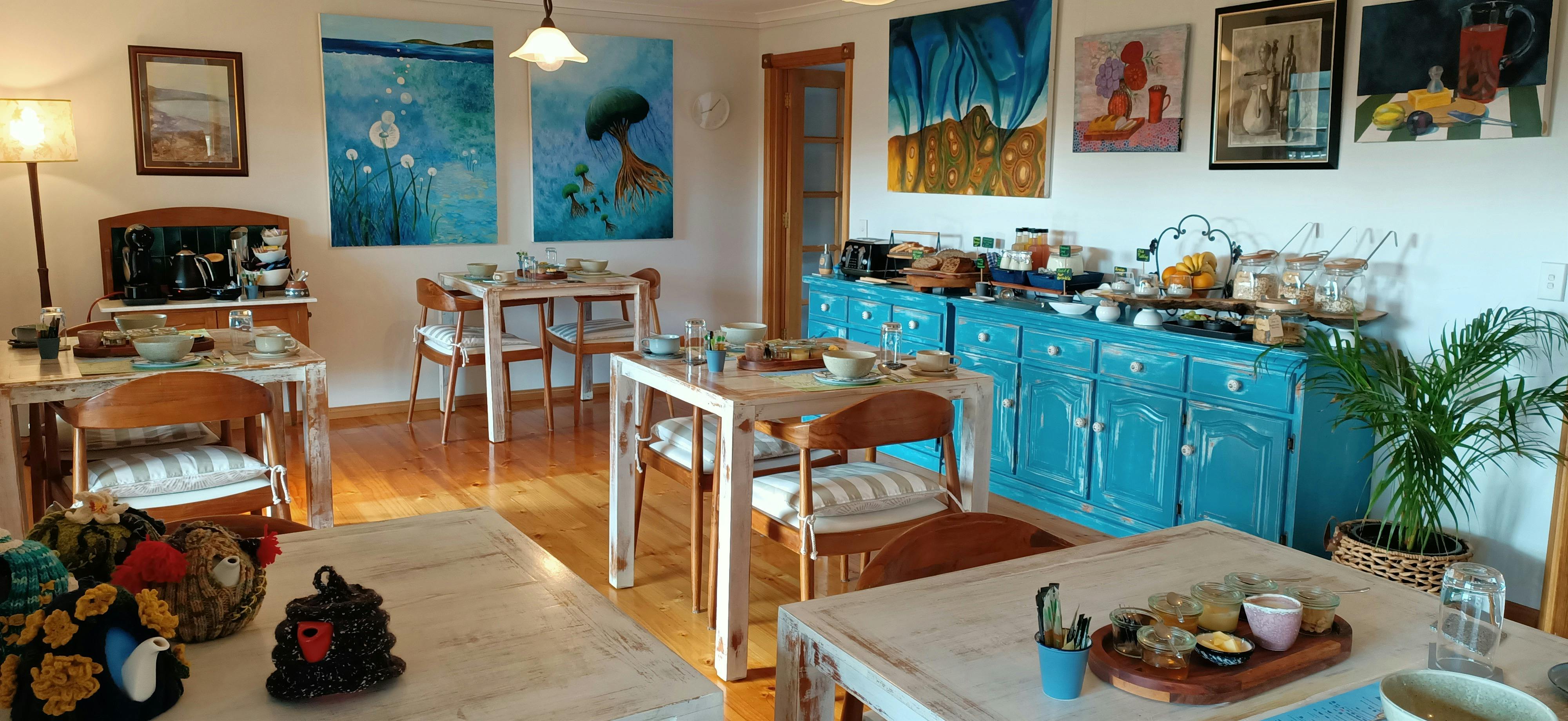 Breakfast set on individual square tables in a light room decorated with original artworks.