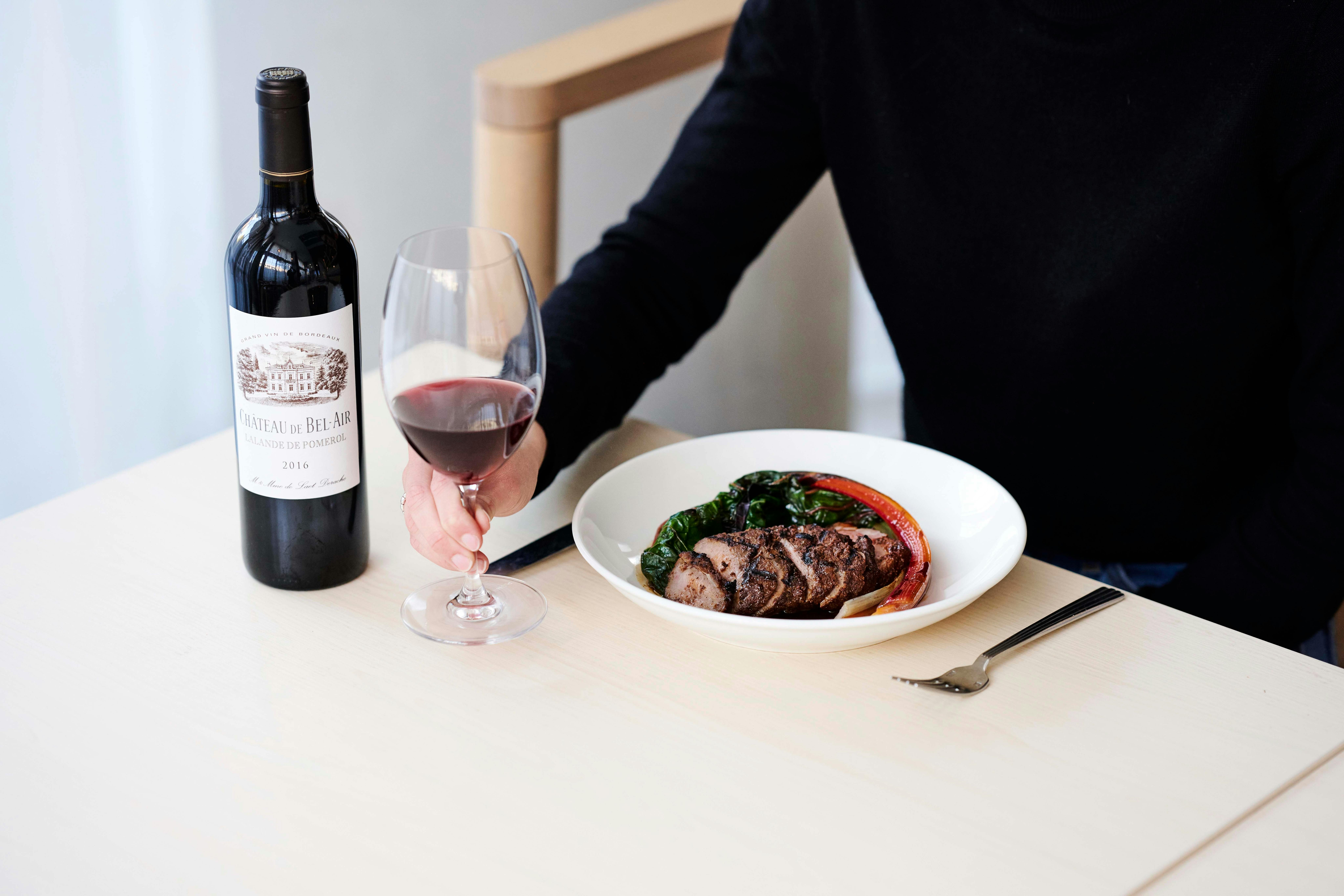 A guest holds a glass of red wine and food.