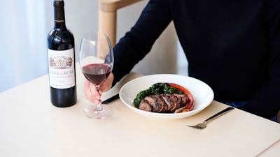 A guest holds a glass of red wine and food.