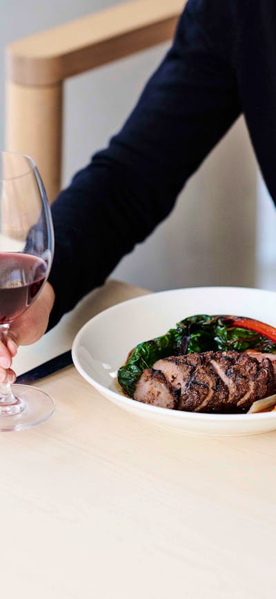 A guest holds a glass of red wine and food.