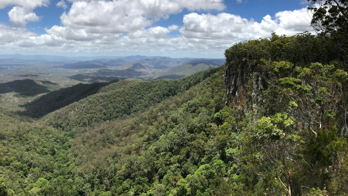 An expansive view over vast green valleys and fluffy white clouds against a light blue sky. An expansive view over vast green valleys and fluffy white clouds against a light blue sky.