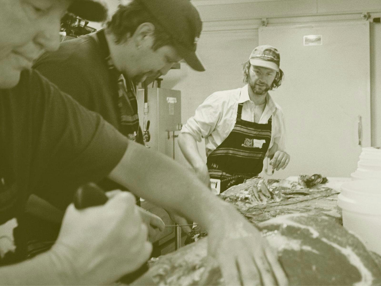 Three men in cool room butchering meat from farm