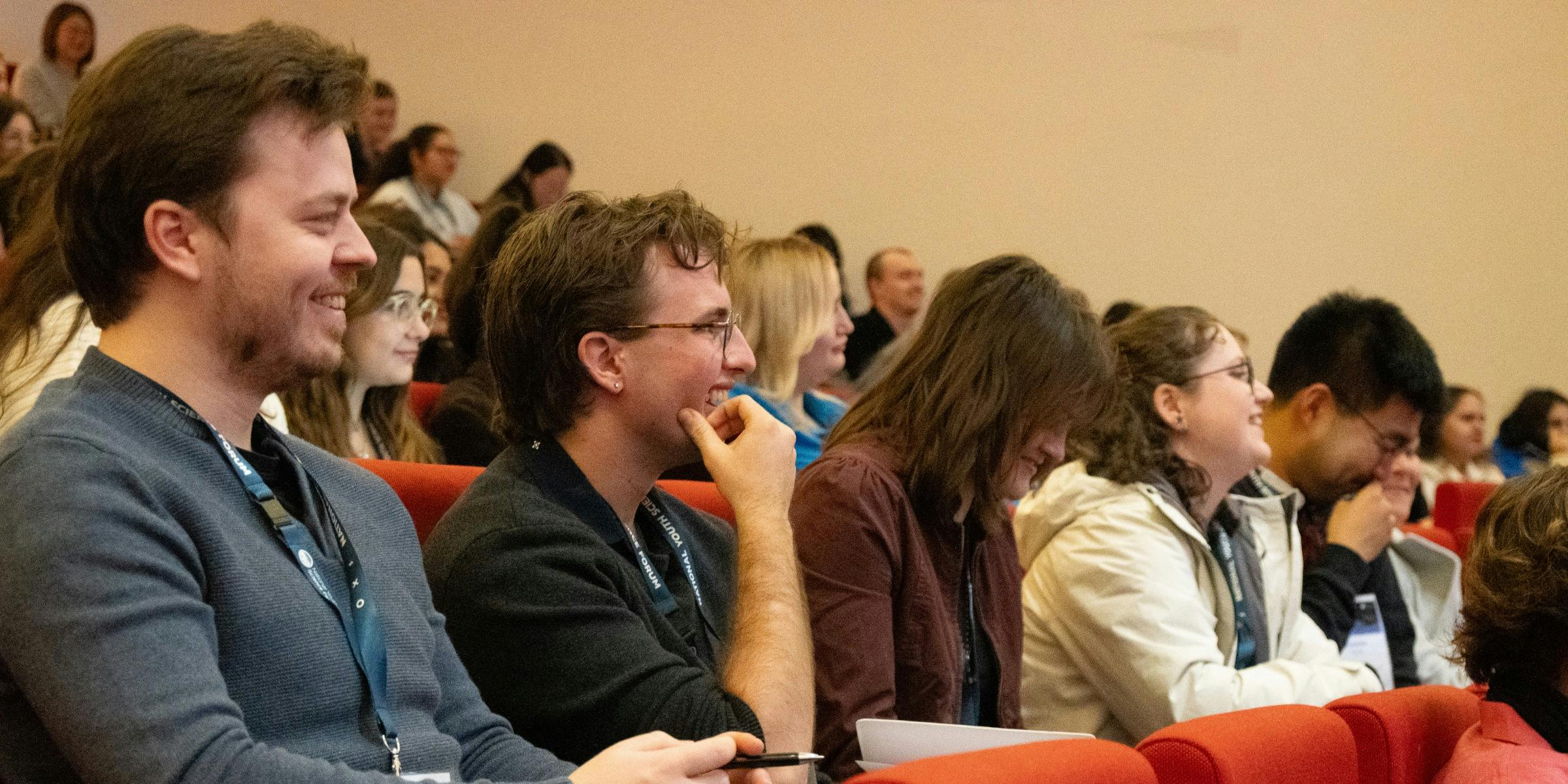 A row of conference attendees, two attendees are seen smiling in the foreground