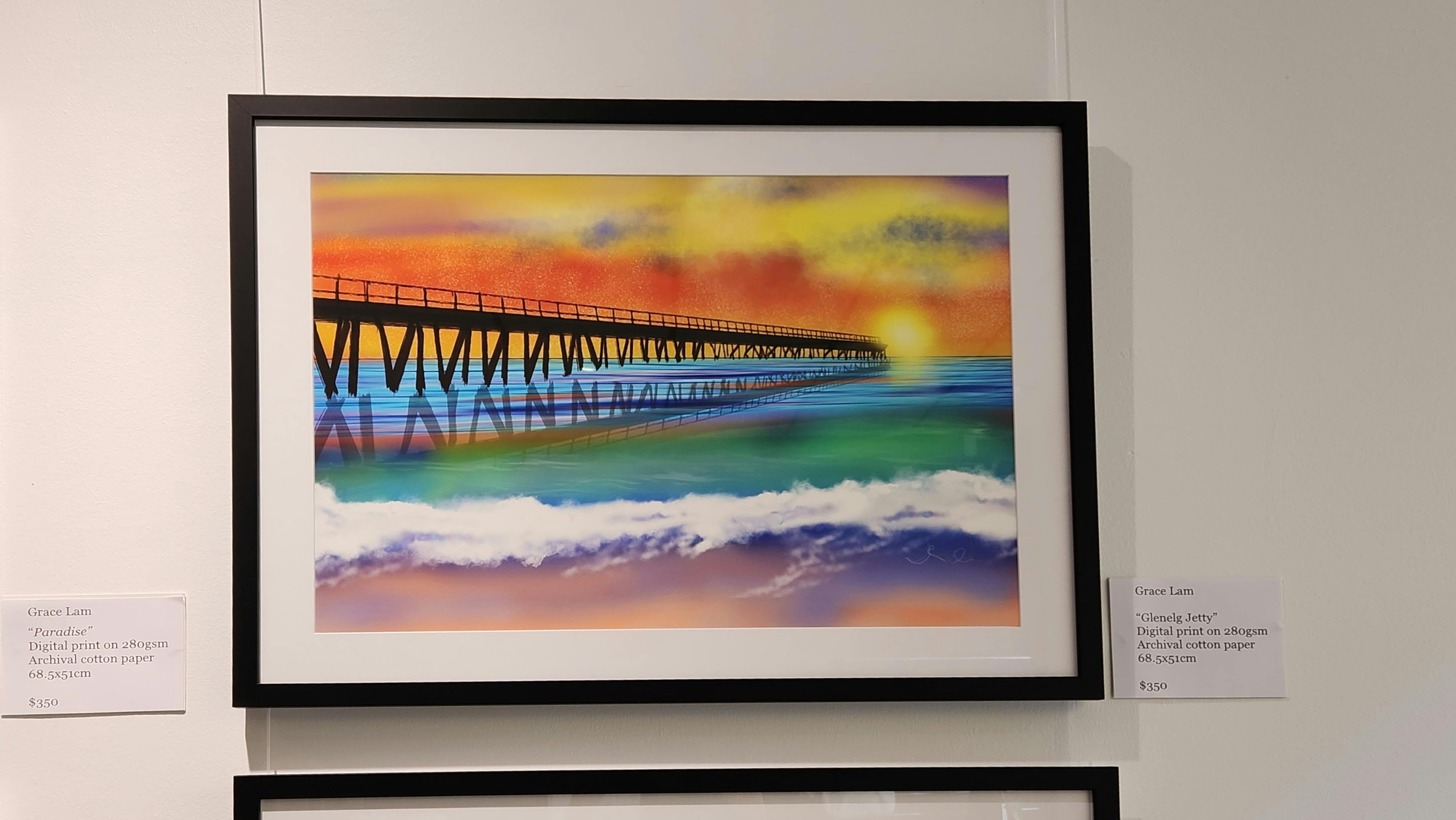 A framed artwork of a jetty at sunset. The  sand and waves in the foreground.