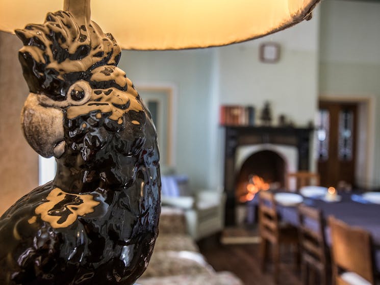 Face of a black cockatoo which is a lamp base, looking to a dining table and open fireplace