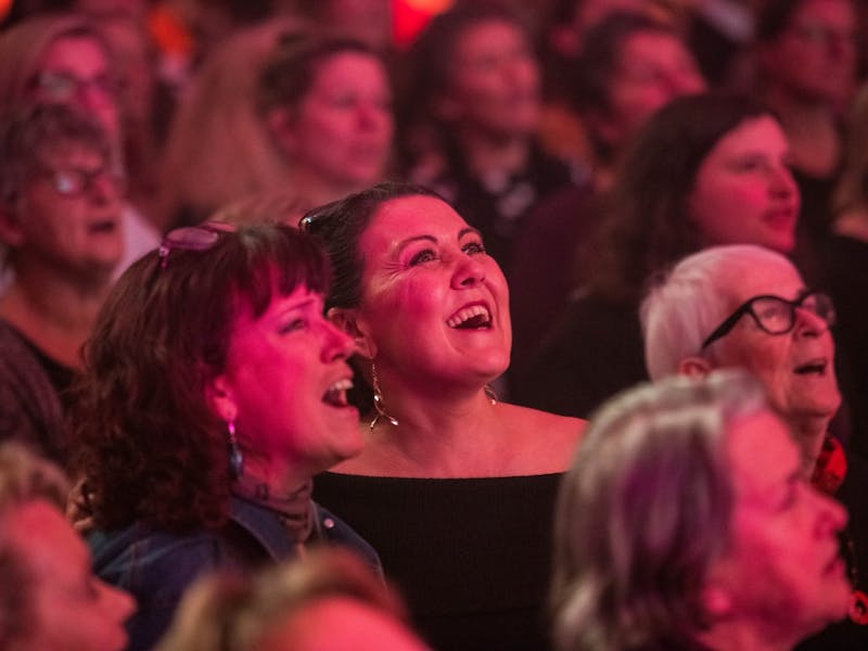 Two women singing  together in a crowd with red light illuminating them