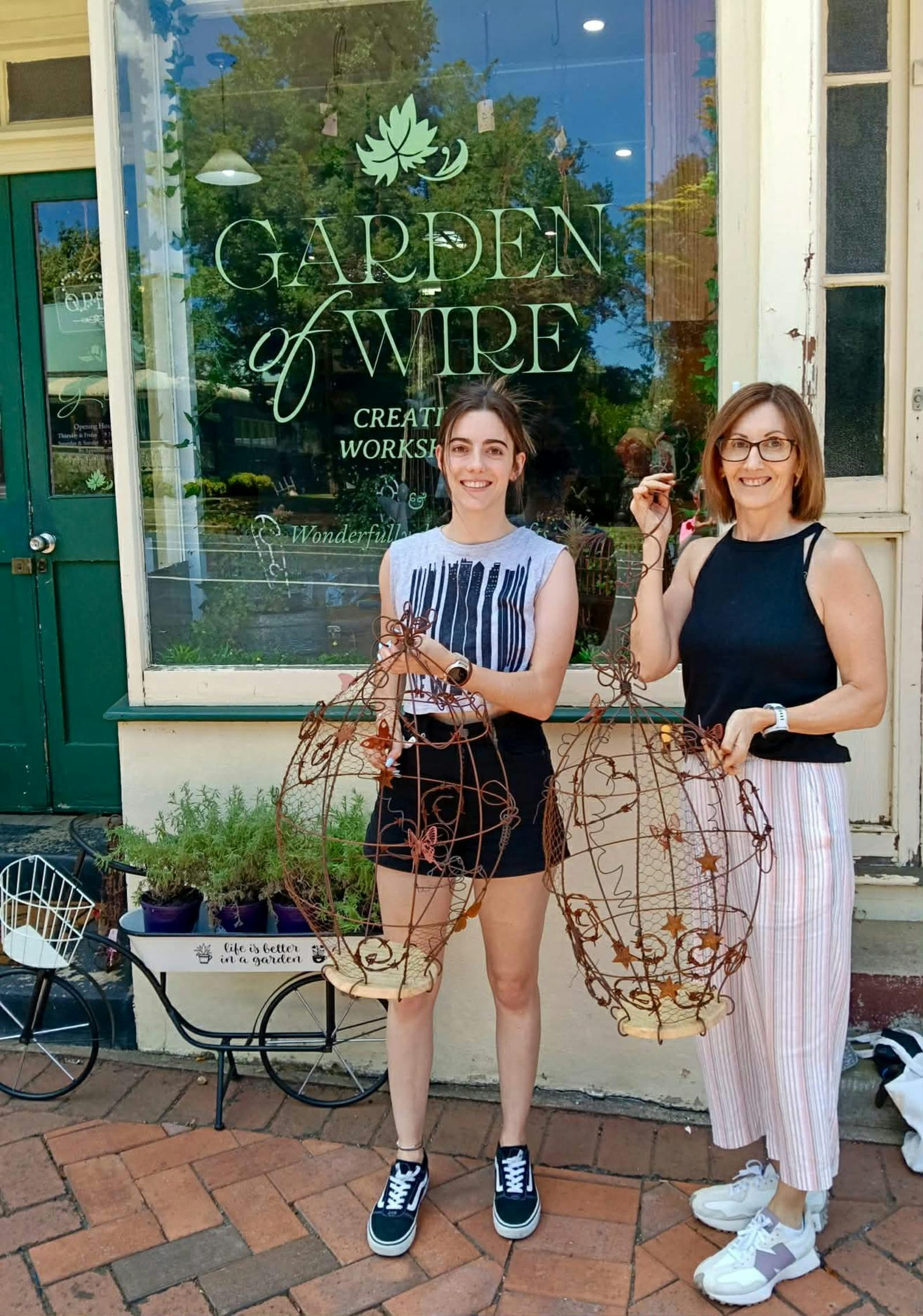Two women in front of the shop with their completed Embellished Birdcage.
