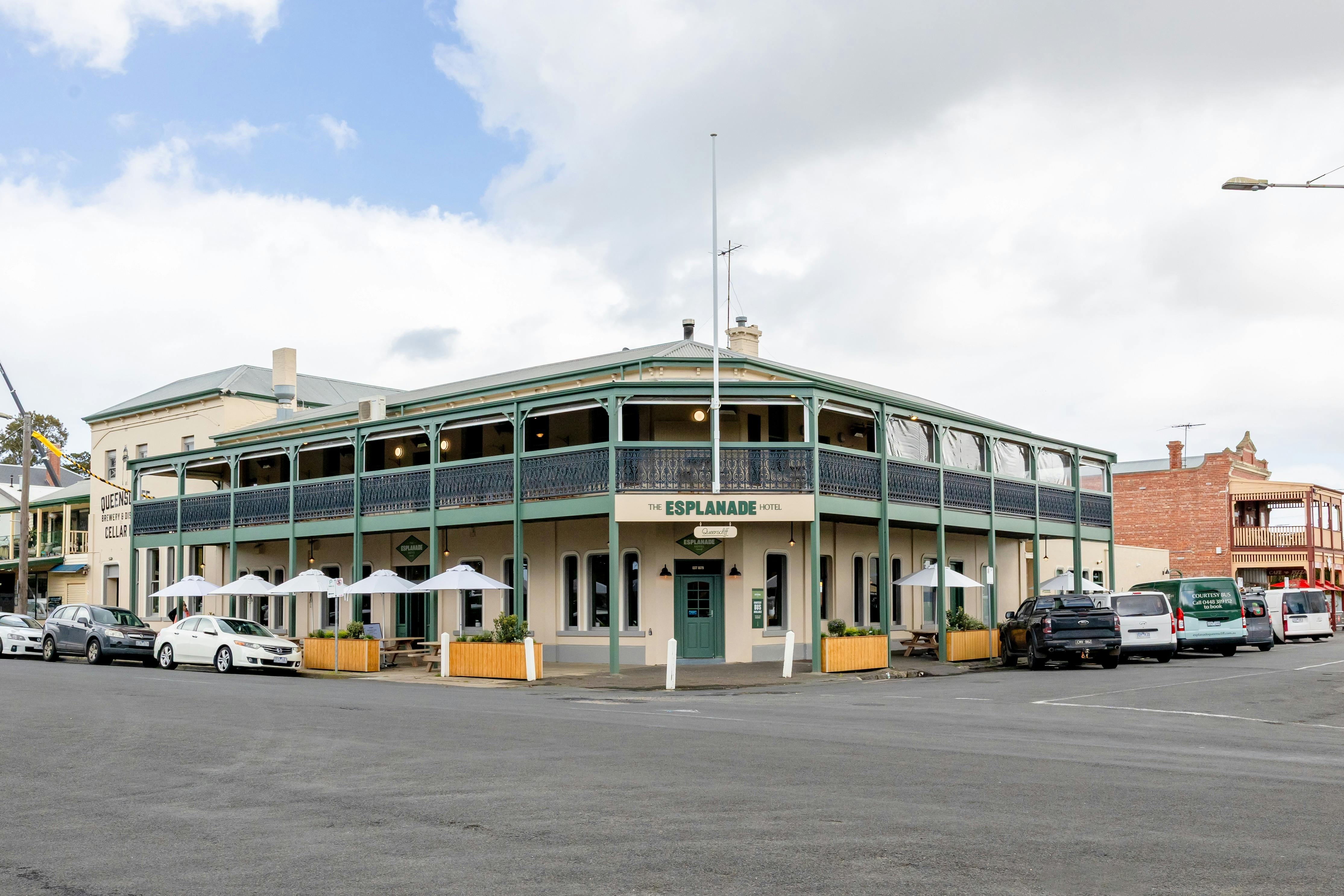 outside of building, cream and green building with umbrellas and tables outisde on the edge