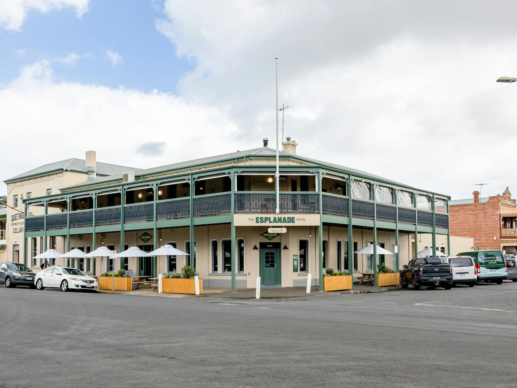 outside of building, cream and green building with umbrellas and tables outisde on the edge