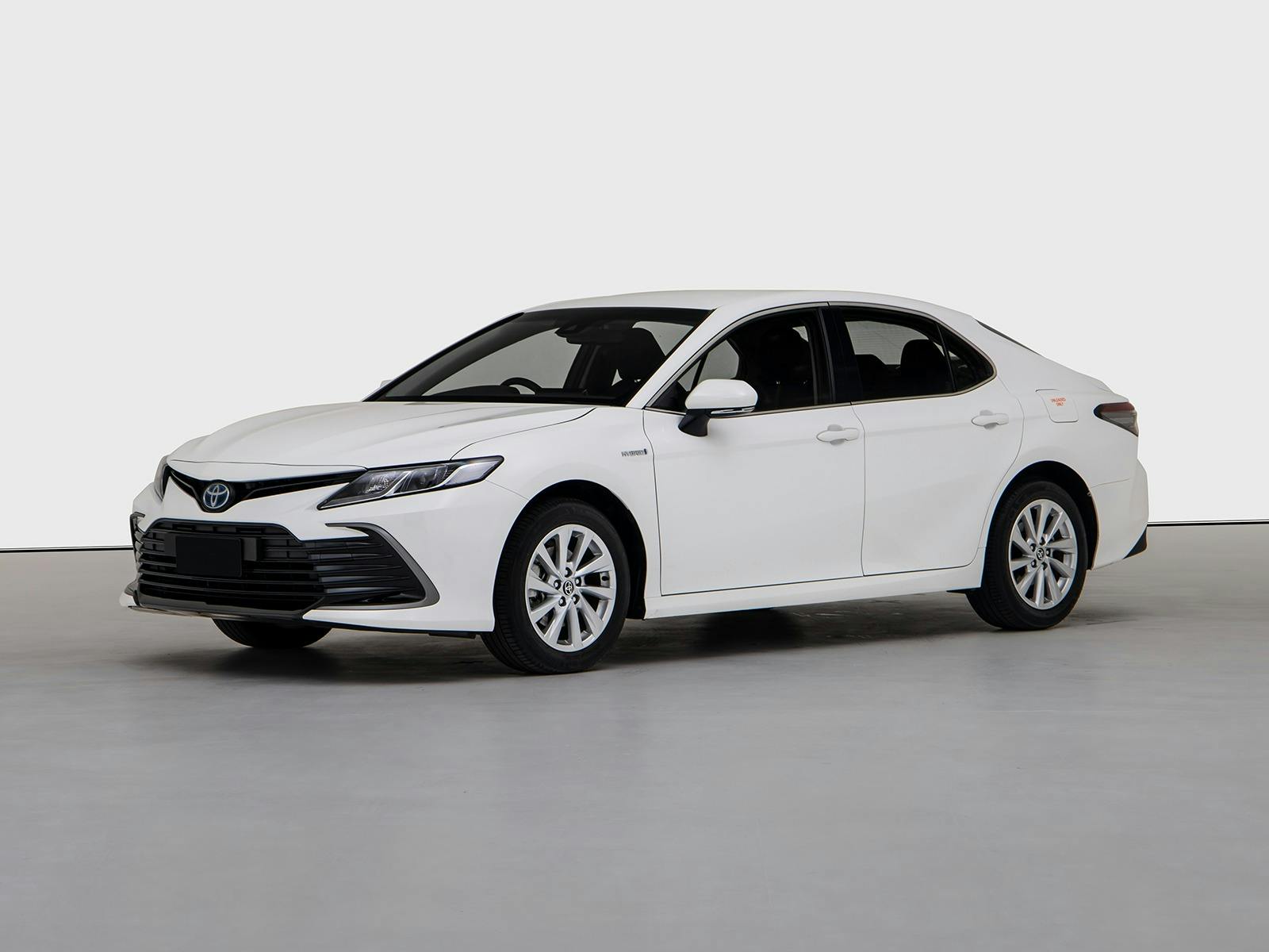 White Toyota Camry Hybrid offered by Orana, shown from the front side on a plain studio background.