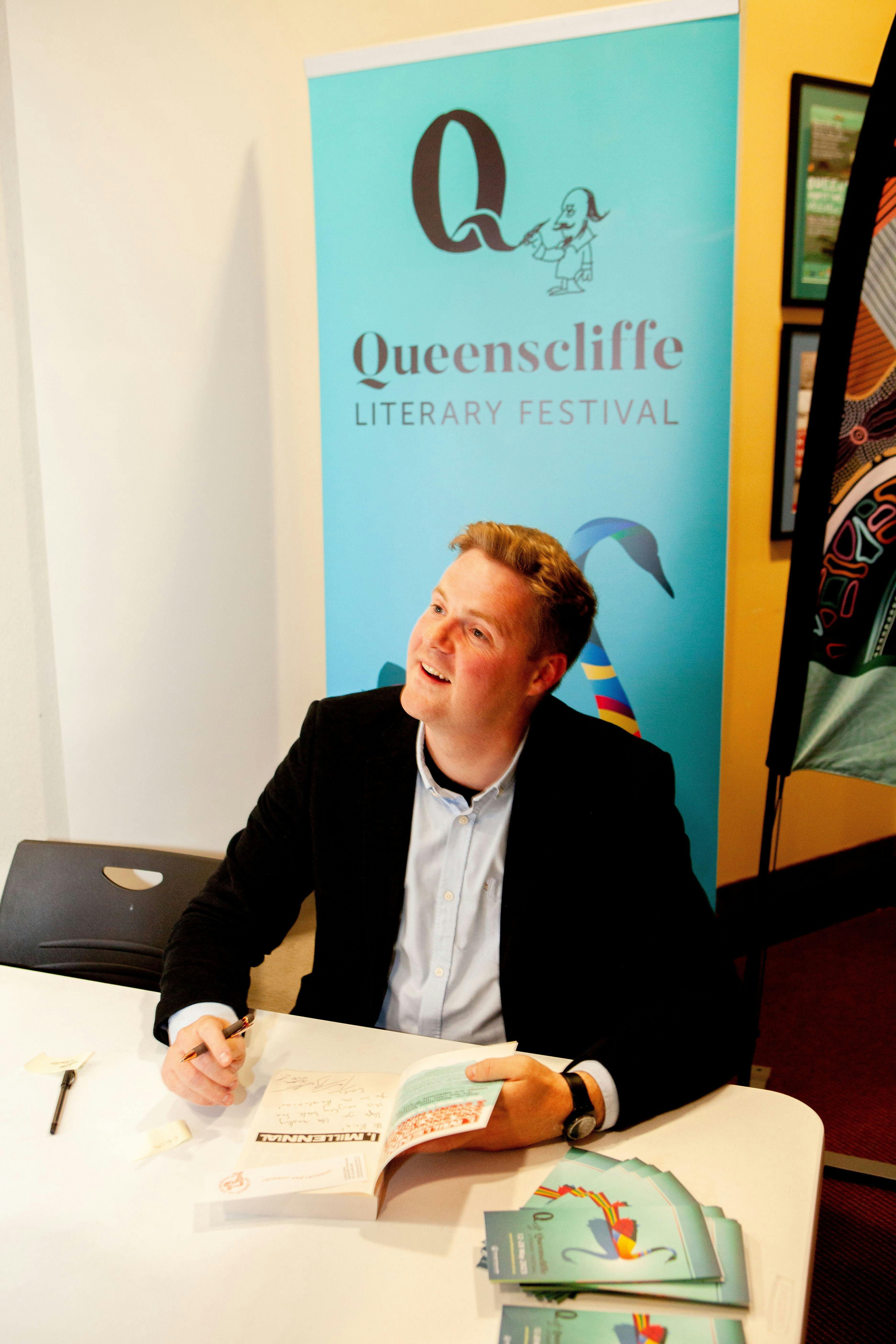 Tom Ballard smiles warmly as he signs his book for an audience member who we cannot see