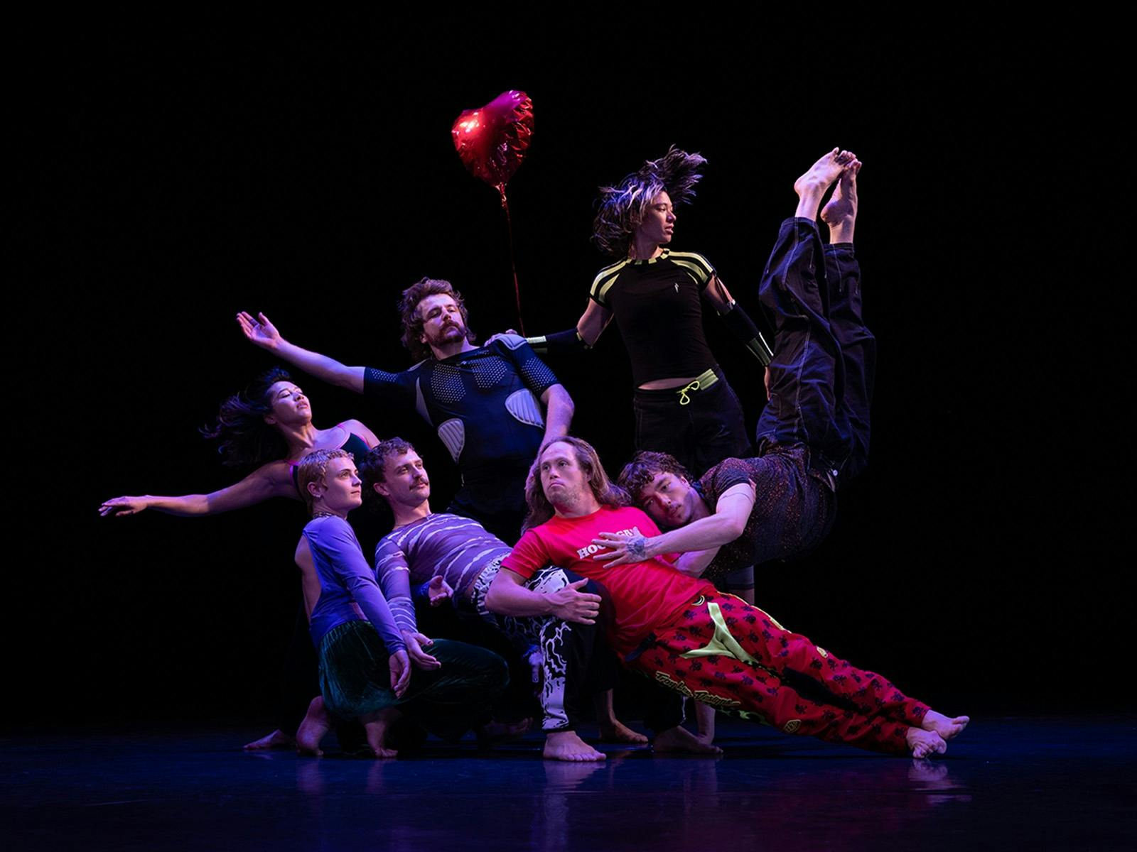 A group of 7 dancers pose against a black background,