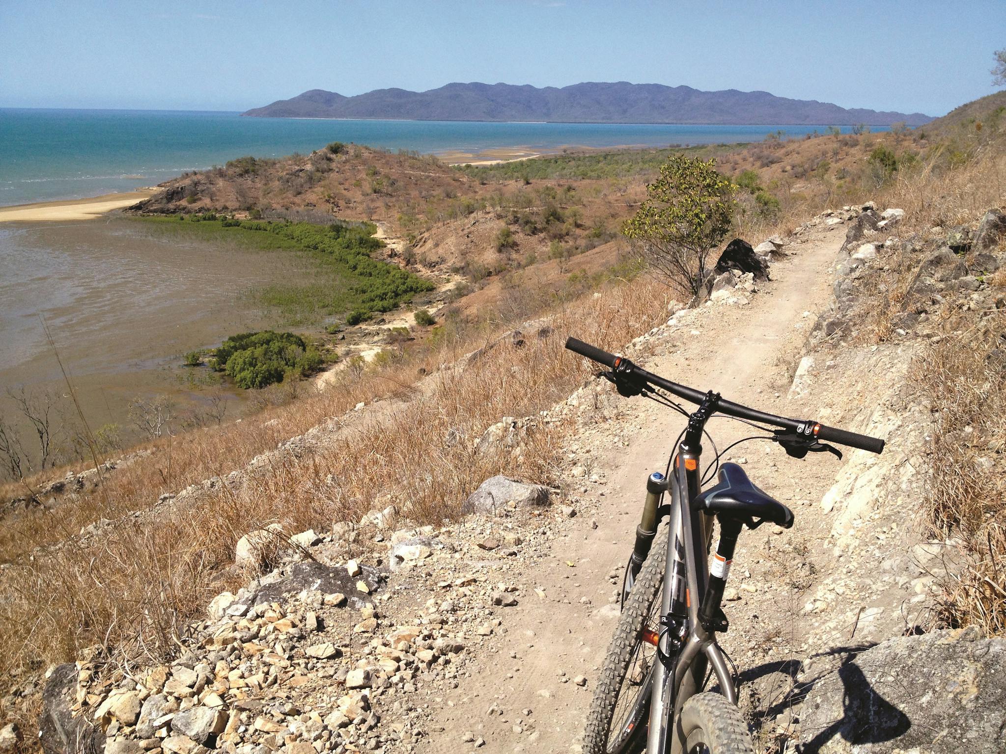 Mountain bike parked on dirt trail winding around a hill slope with a view over headland, ocean Mountain bike parked on dirt trail winding around a hill slope with a view over headland, ocean