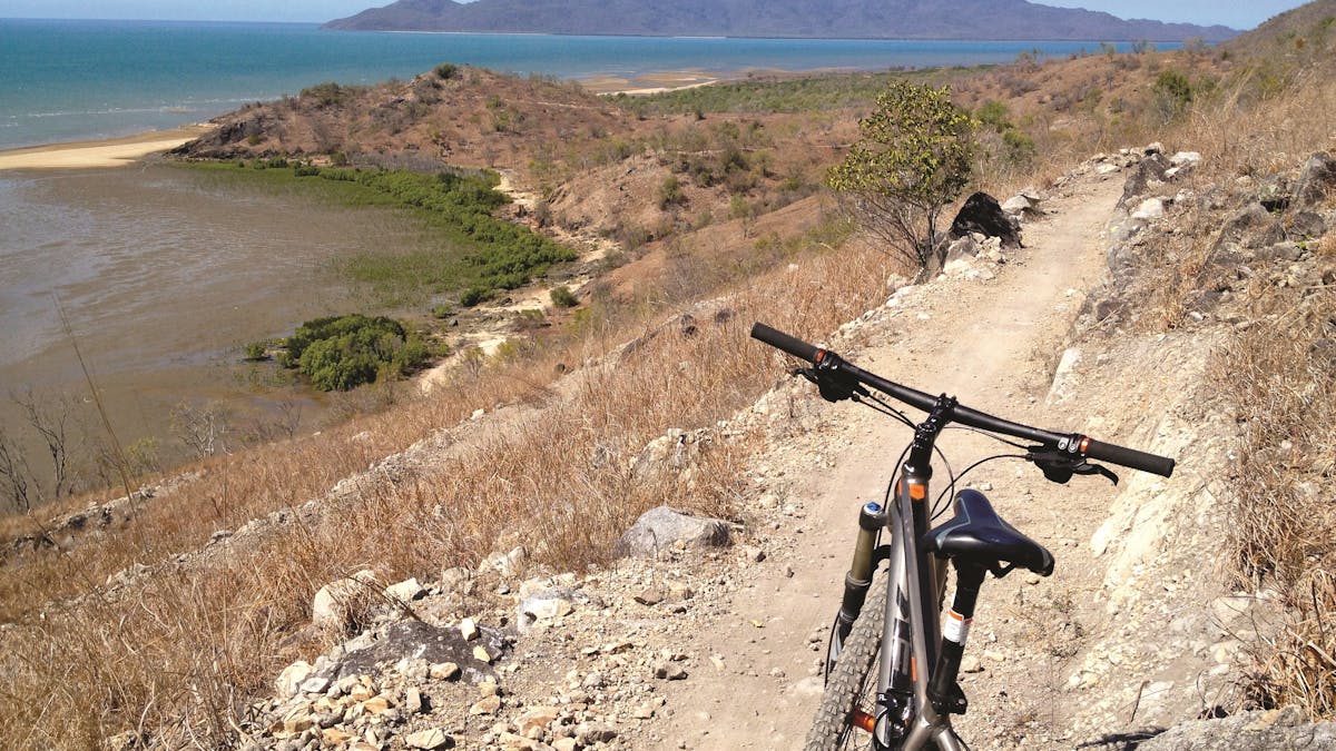 Mountain bike parked on dirt trail winding around a hill slope with a view over headland, ocean