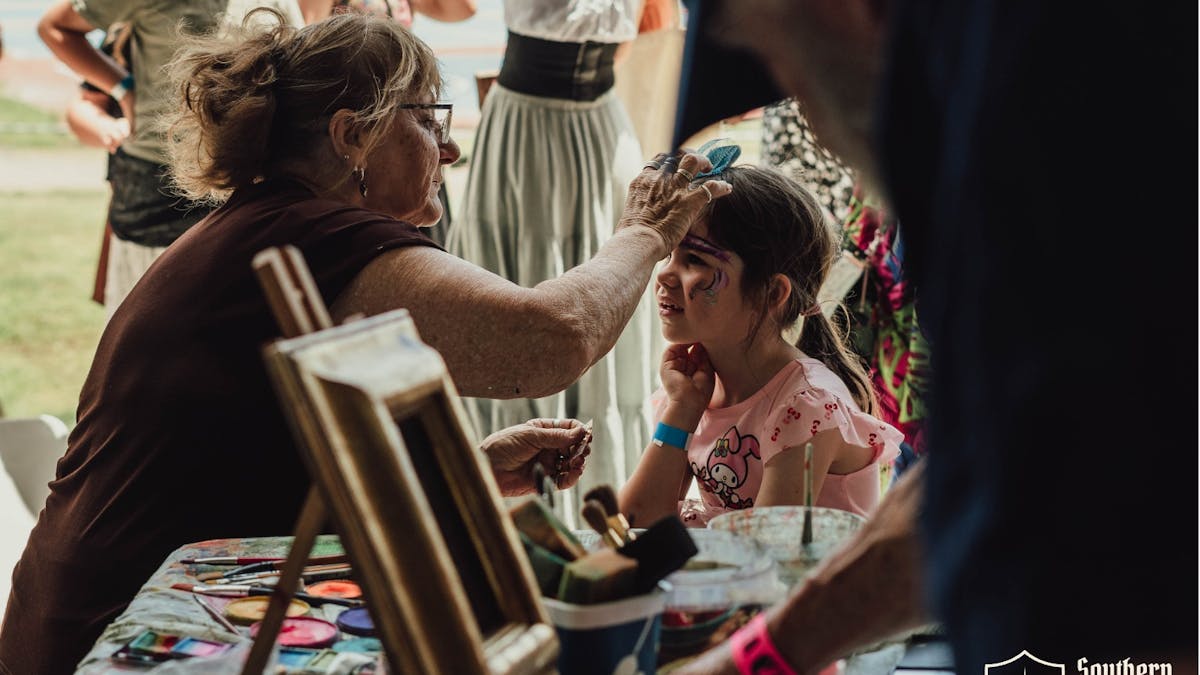 Young girl getting her face painted at a family-friendly stall at Southern Realm Festival.