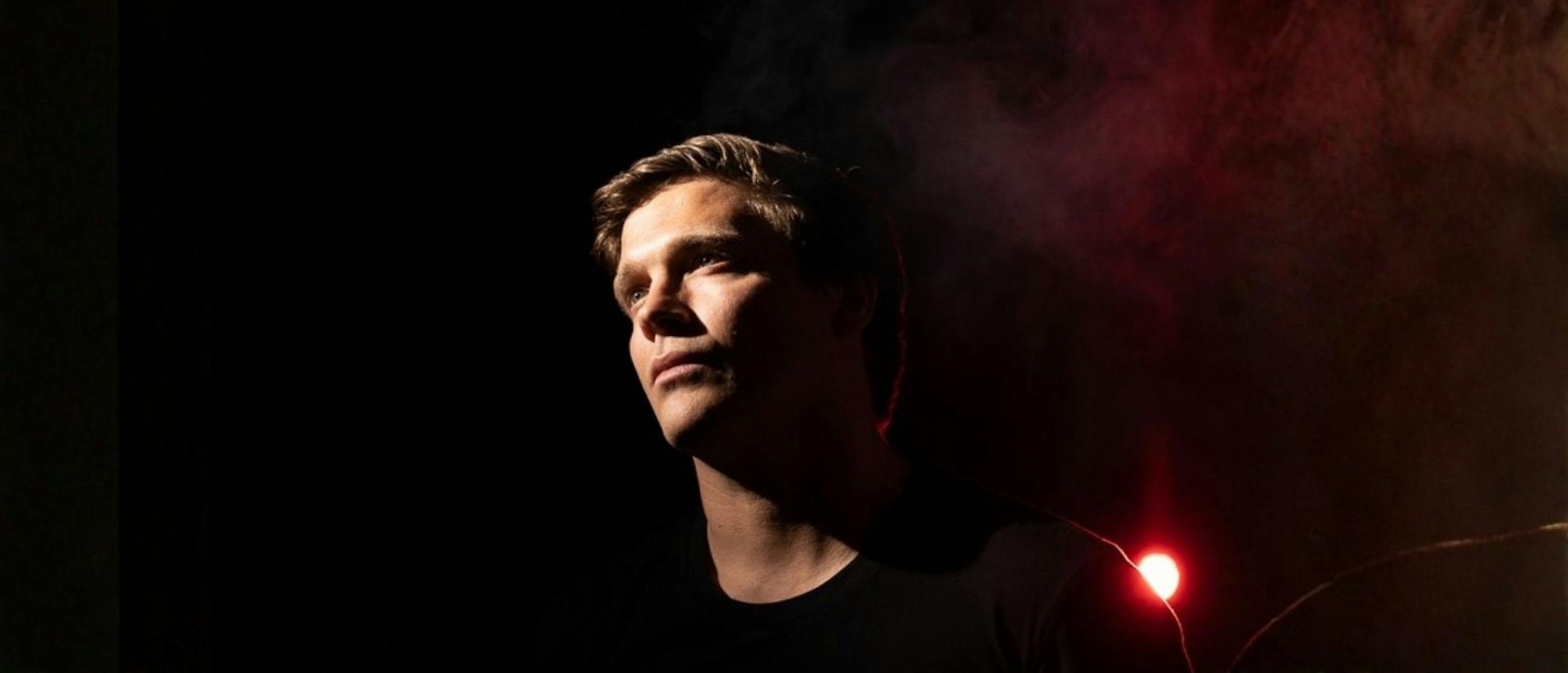 A headshot of the artist, a man with blonde hair wearing a black top looking into the distance.