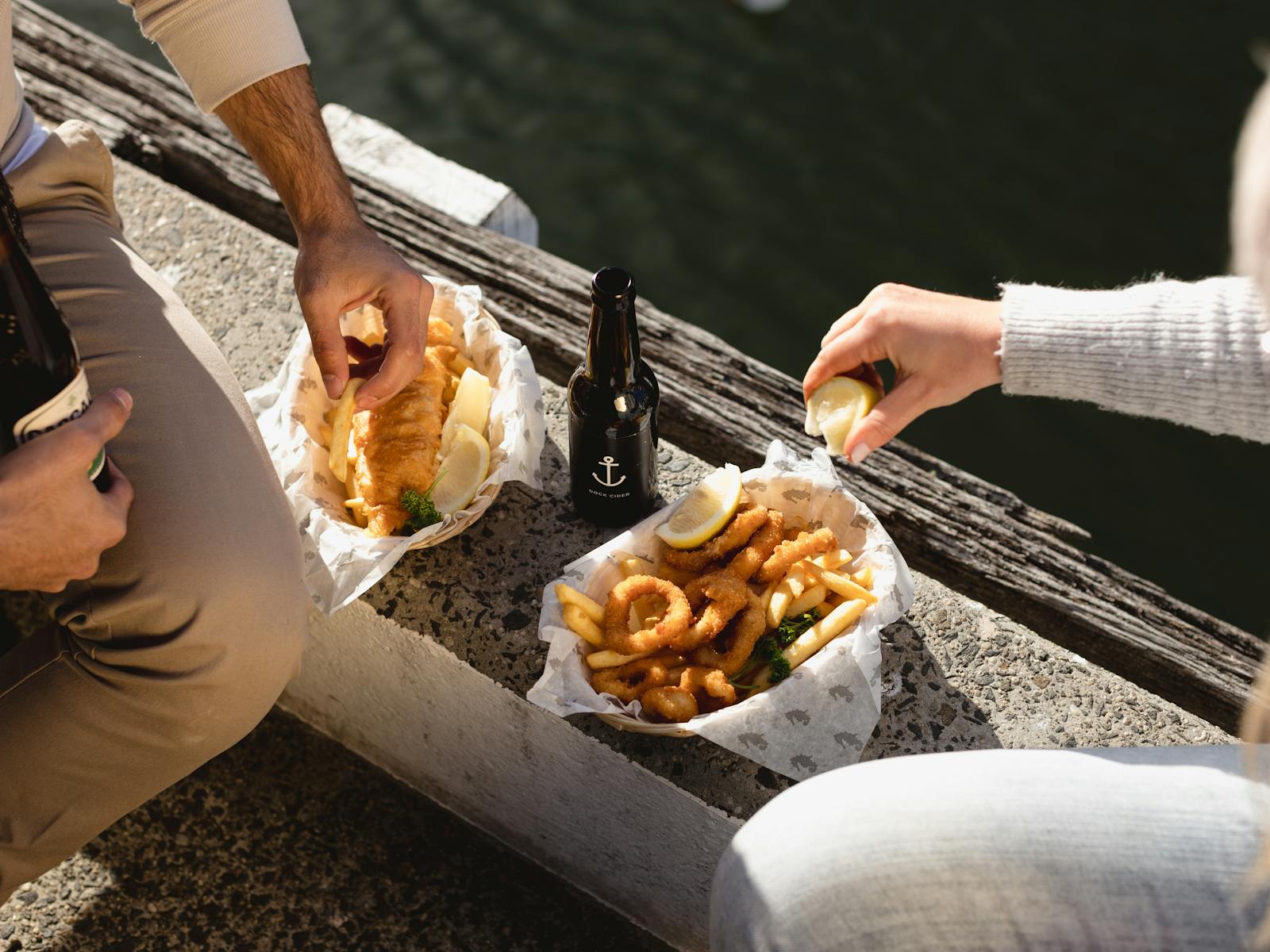Two people enjoying fish and chips on the side of the dock outside Mures Lower Deck.