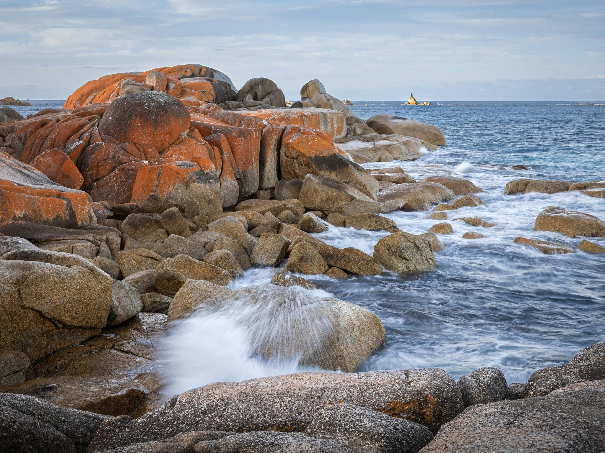waves crashing in on rocky coastline - rocks covered in orange lichen