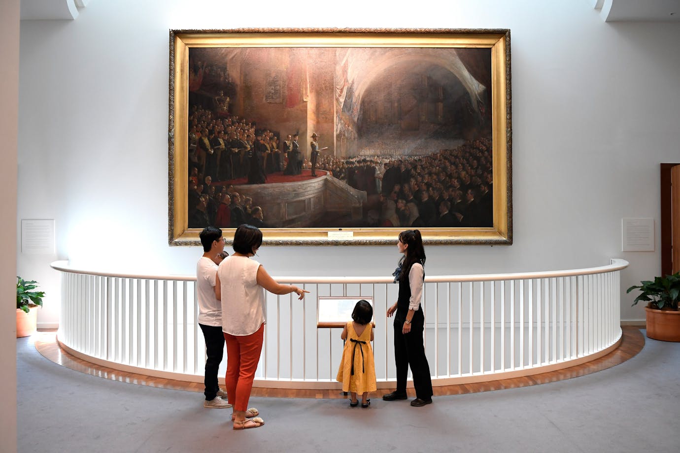 Visitors stand on an upper level of Parliament House, viewing a large framed historical painting.