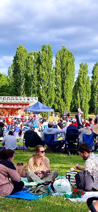 people sitting on a grass field watching Carols in Town Park Canberra