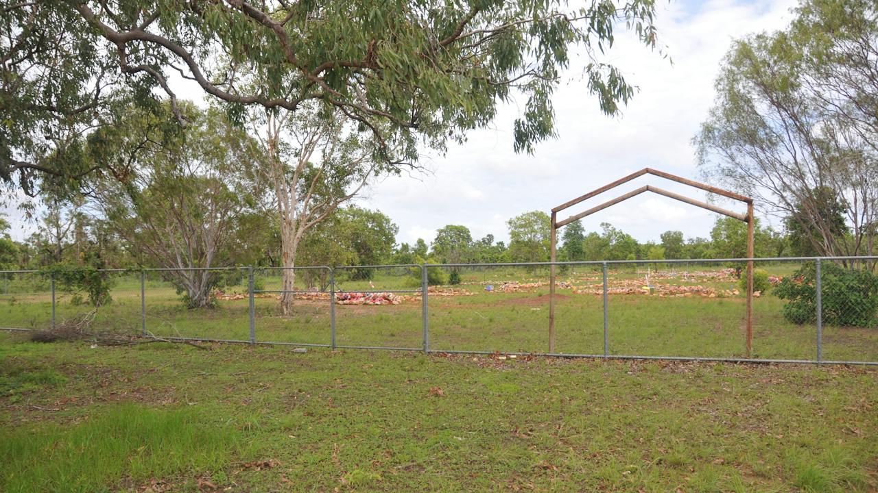 Cemetery entrance marked by a steel portal structure that appears considerably older than the fence.