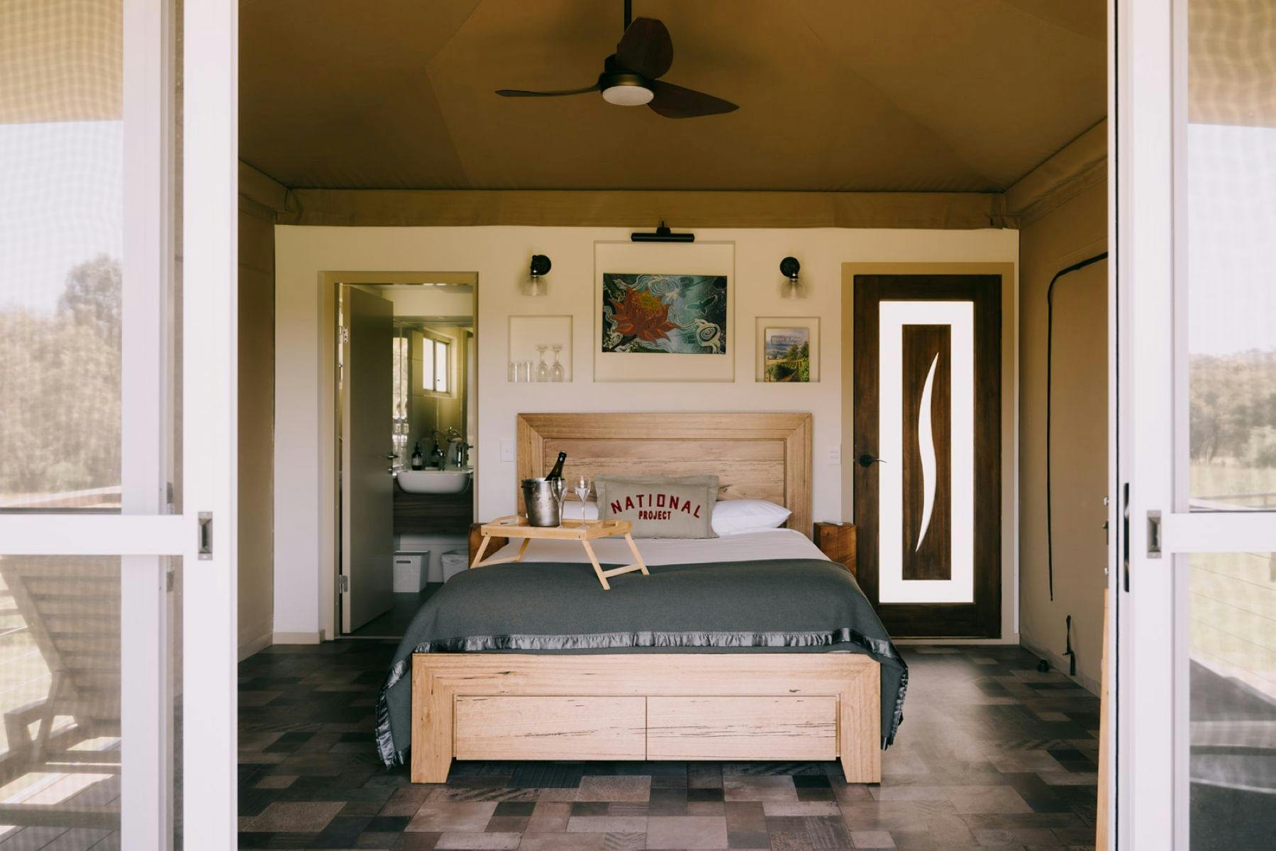 Luxury tent interior with a wooden bed, stylish decor, and open view of nature through sliding doors