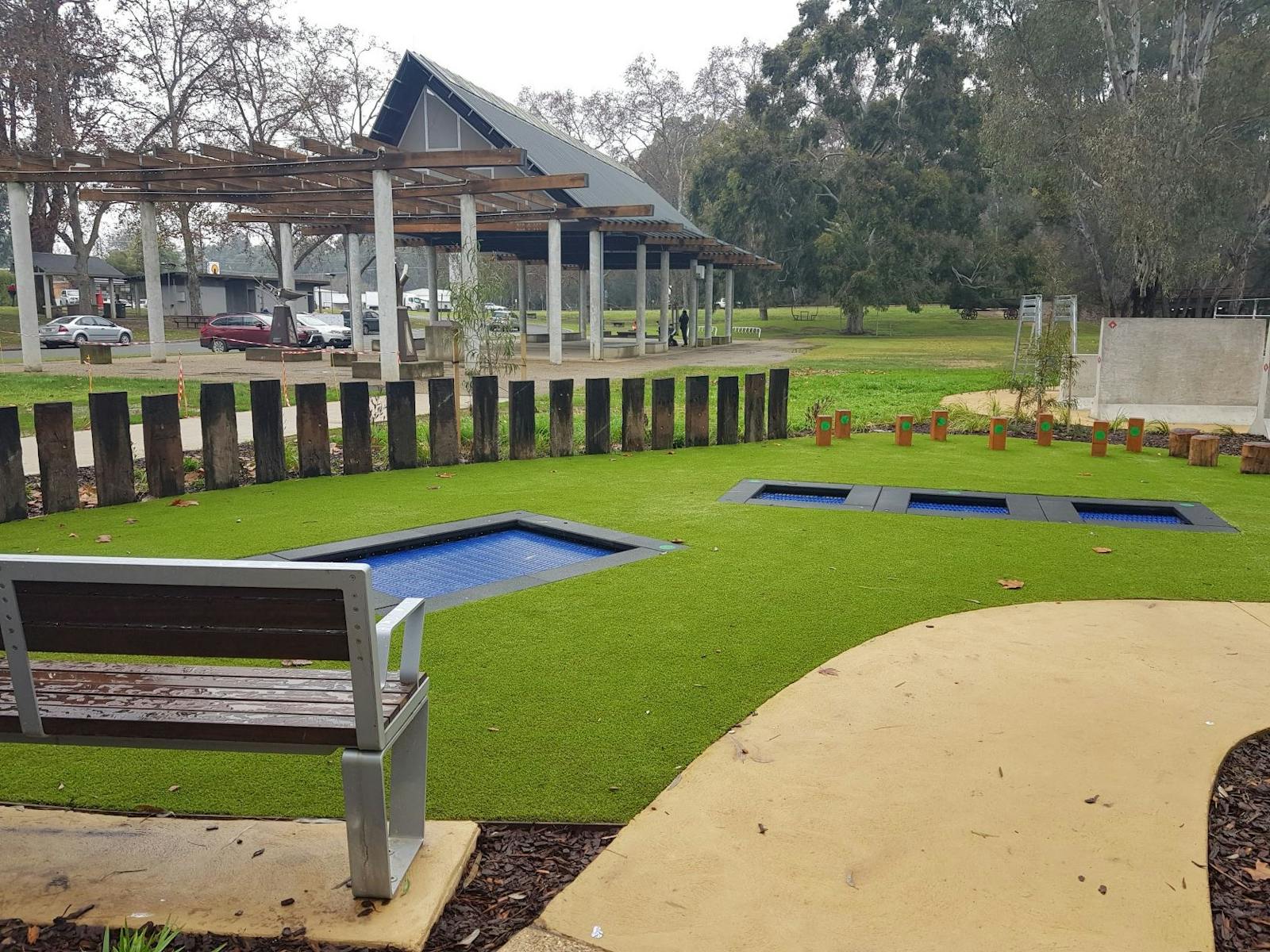 seat, grass, square trampolines in ground, stepping logs, path, fencing, pavillion
