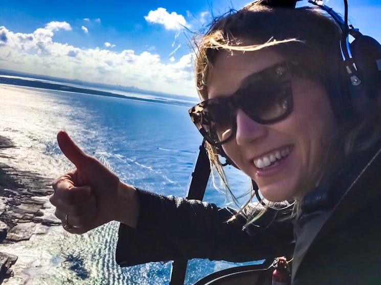 Smiling passenger on a doors-off helicopter flight with coastline in background