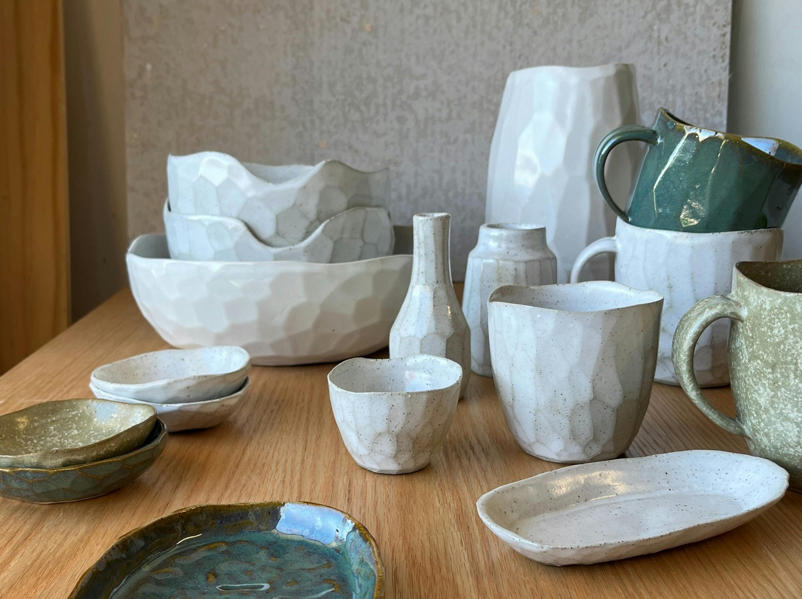 身穿绿色衬衫和眼镜的女人微笑着看着手里的杯子，身后是架子上的花盆