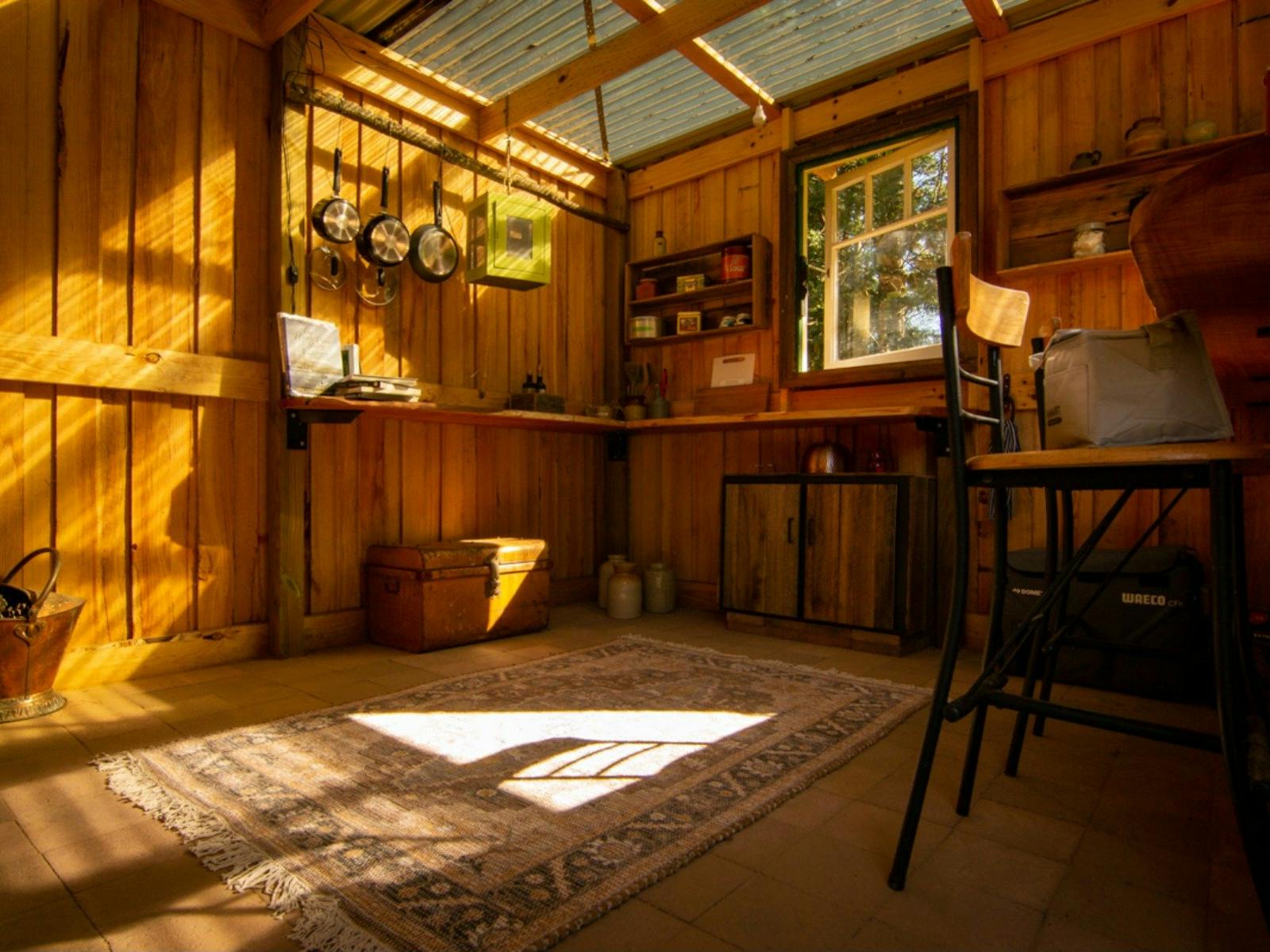 Rustic camp kitchen space with benches, stool seating, cupboards and kitchen equipment.
