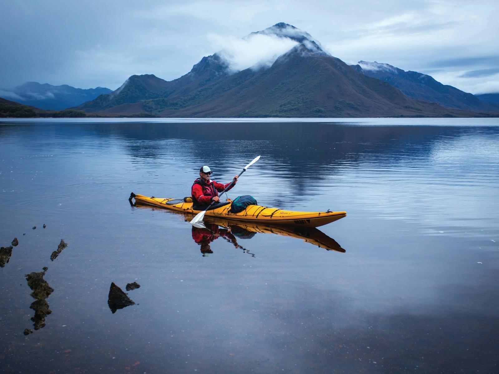 Kayaker on Bathurst Harbour with Mt Rugby in the distance