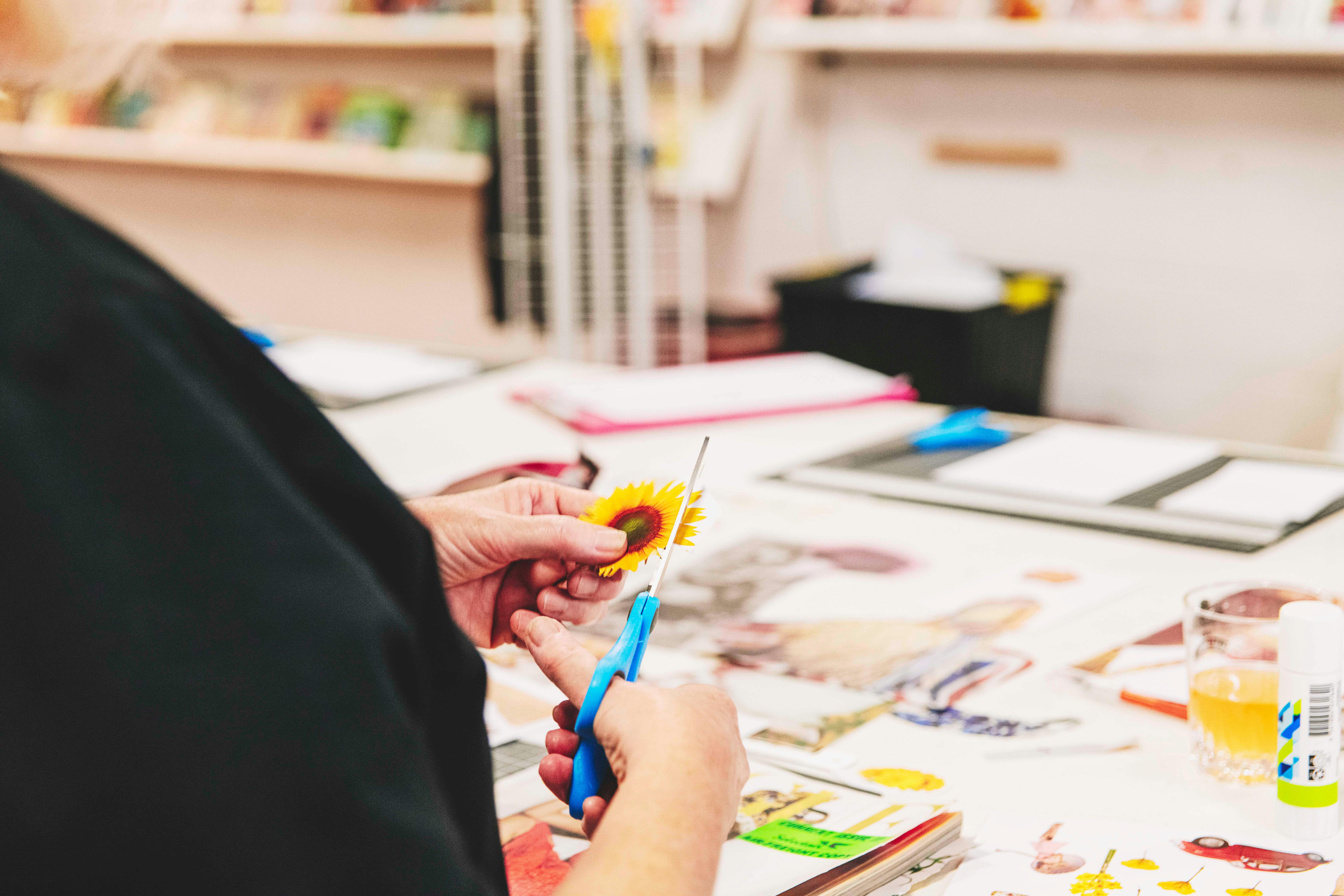 Eine Person schneidet und klebt Elemente aus Zeitschriften und Vintage-Dokumenten auf den Tisch.