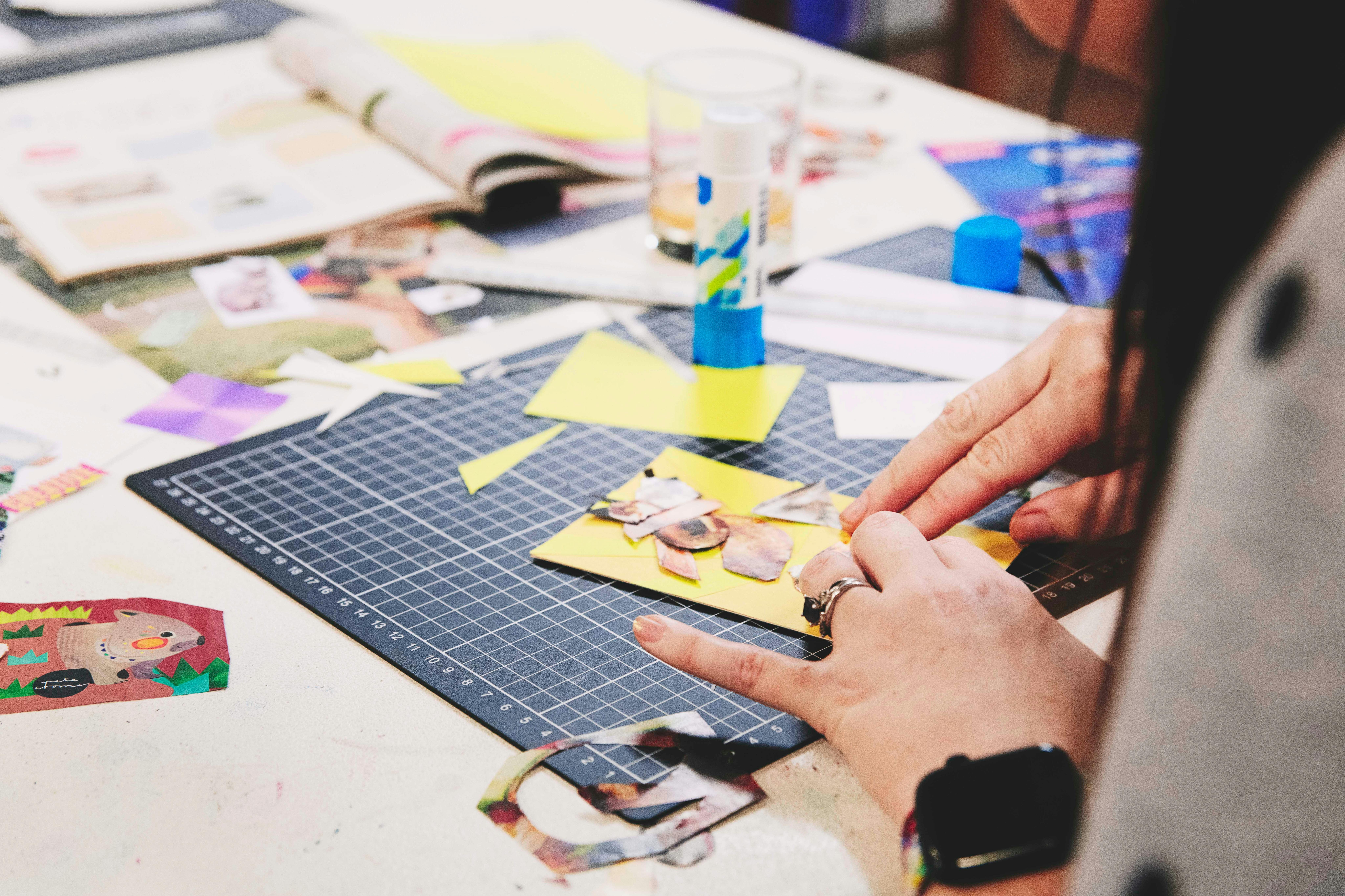 Eine Person schneidet und klebt Elemente aus Zeitschriften und Vintage-Dokumenten auf den Tisch.