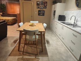 Kitchen table, sink, air fryer, microwave, bed in the background, wooden slat horizontalblinds.