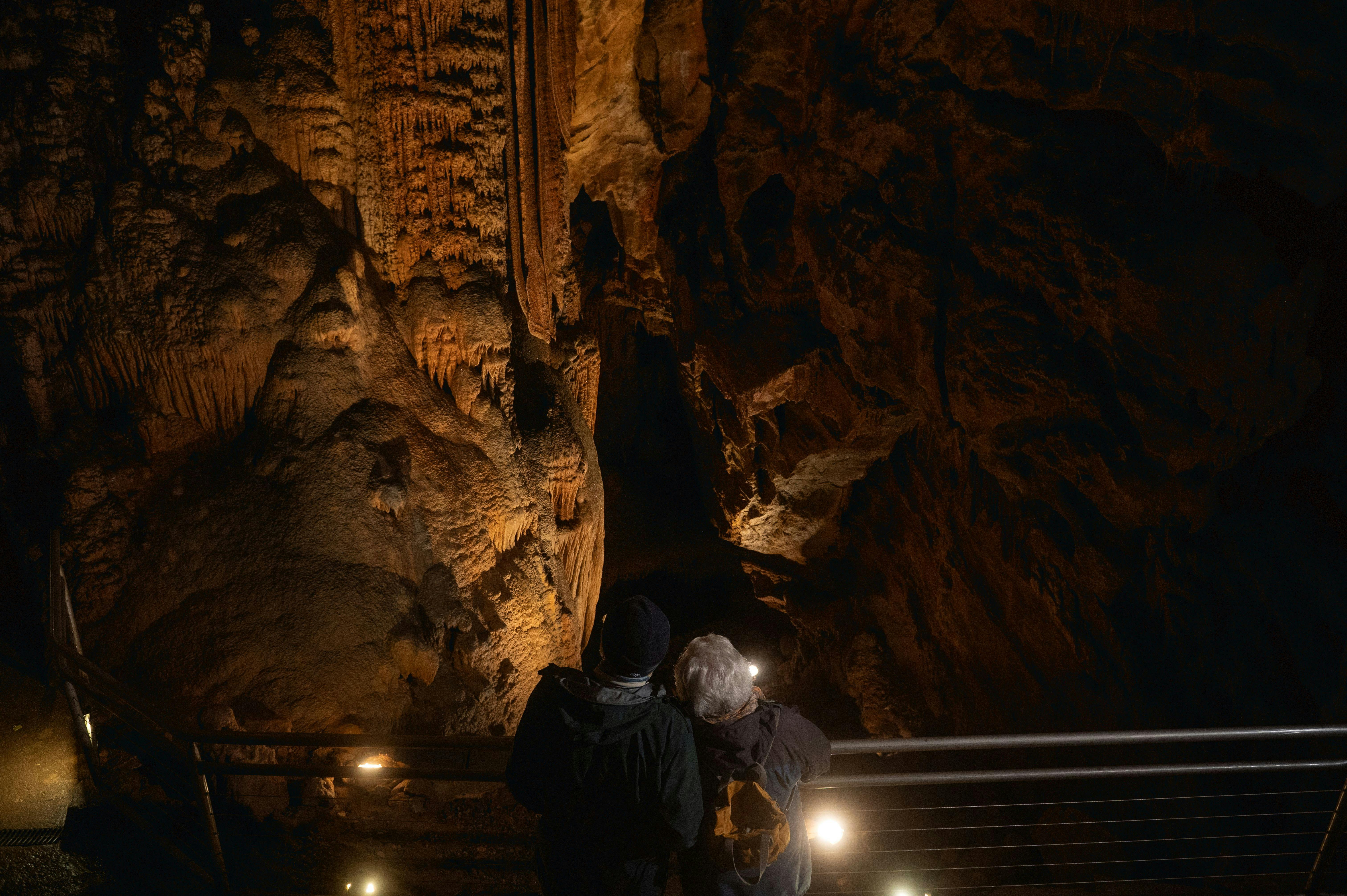 two people standing behind a railing looking out into a large cave interior and formations